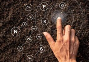 The hands of men are touching on the soil where abundance and technology are icons about the elements and nutrients in the soil around.